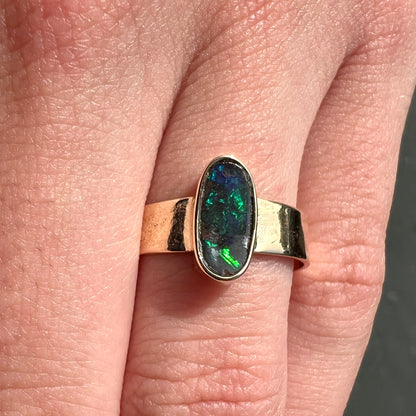 A blue green oval cabochon cut Australian boulder opal set in a yellow gold solitaire ring.