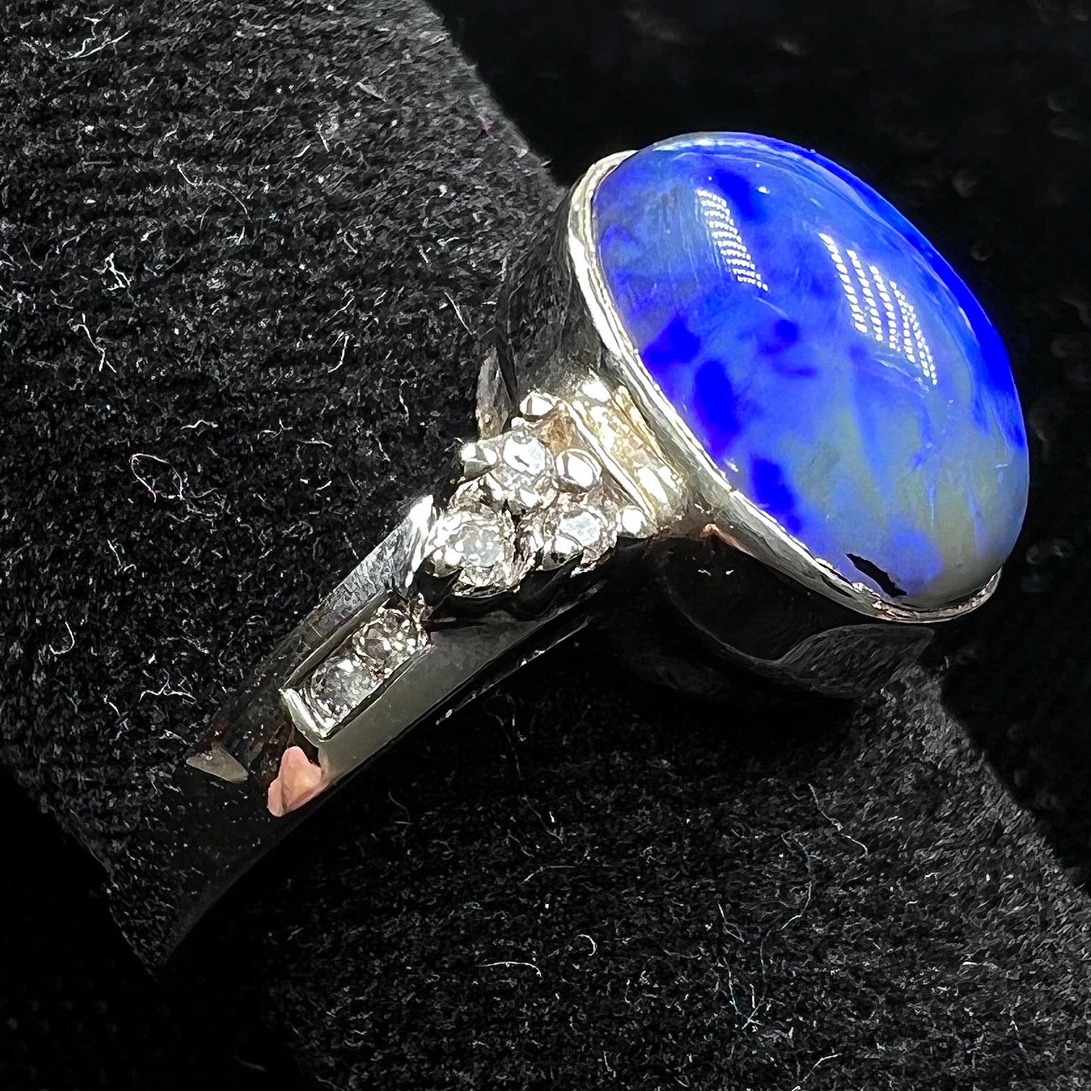 A white gold ring set with a Lightning Ridge black opal and diamond accents.  The opal displays a cat's eye pattern.