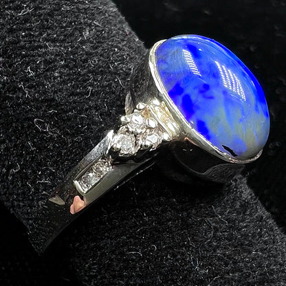 A white gold ring set with a Lightning Ridge black opal and diamond accents.  The opal displays a cat's eye pattern.