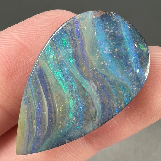 A loose, pear shaped boulder opal stone from Quilpie, Australia.  The stone is predominantly blue, green, and purple with red and orange undertones.