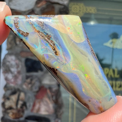 A freeform shaped, polished boulder opal stone from Queensland, Australia.  The stone has red, orange, green, and blue fire.