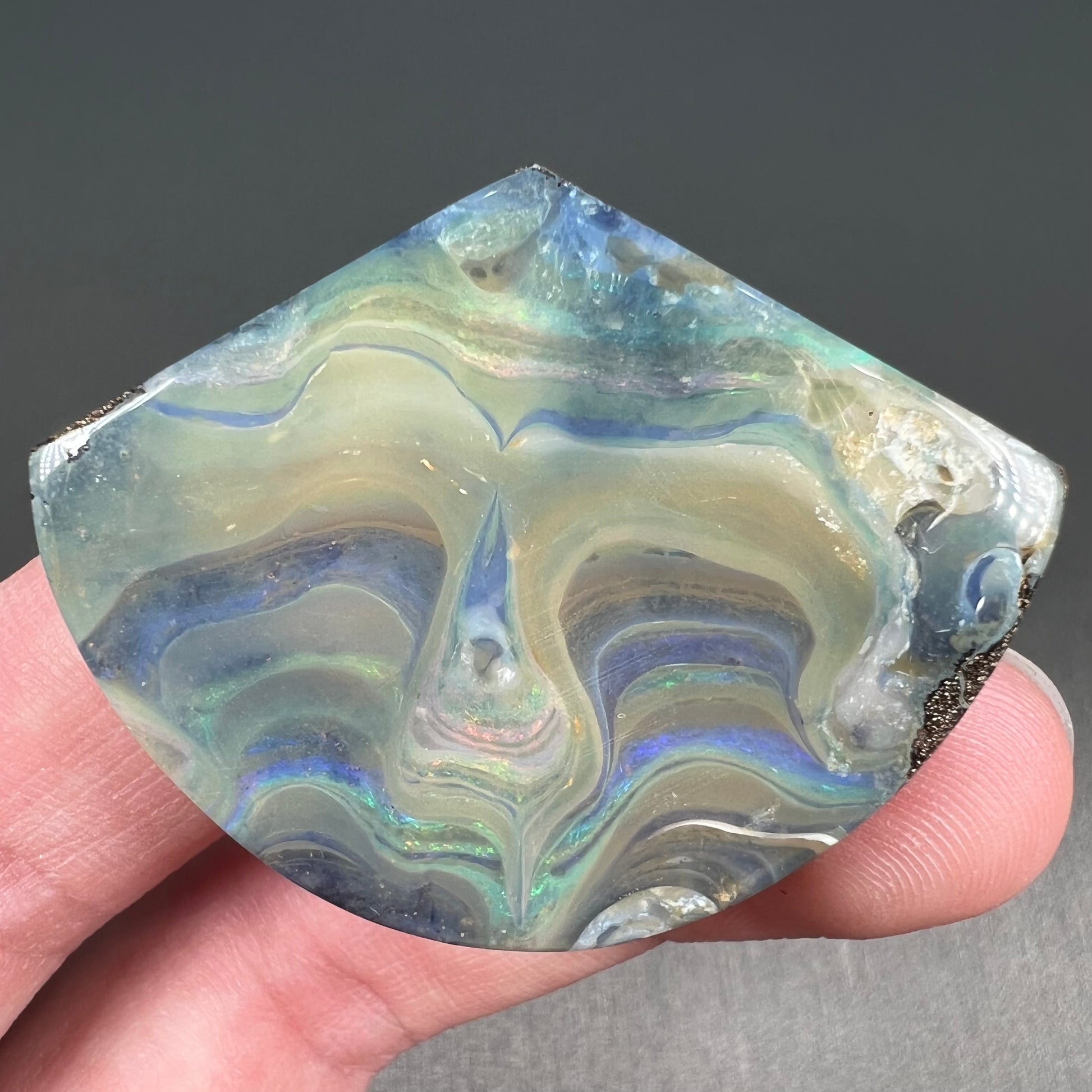 A polished, loose boulder opal stone from Queensland, Australia.  Fire colors are green, blue, purple, and salmon.