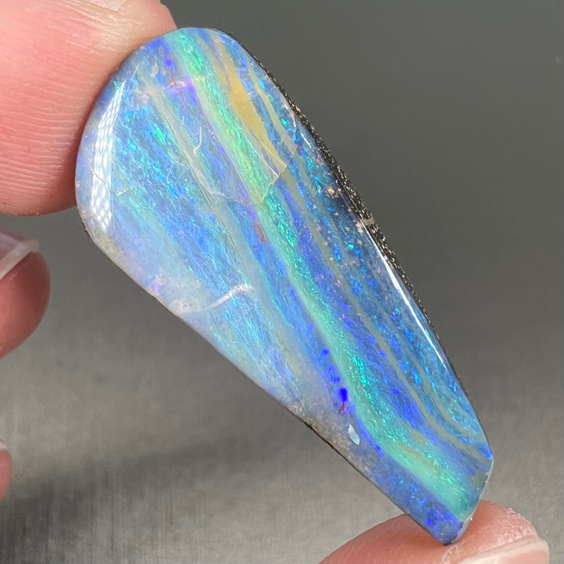 A loose, polished, freeform drop shaped boulder opal stone from Quilpie, Australia.