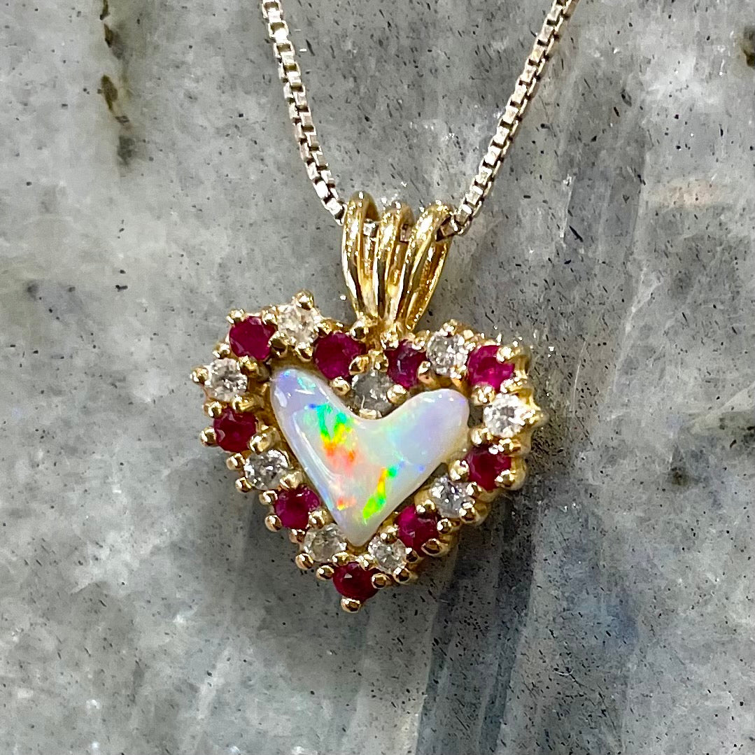 A yellow gold pendant set with a heart cut white opal in a halo of alternating round rubies and diamonds.