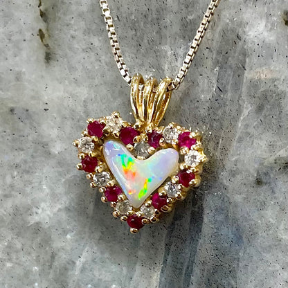 A yellow gold pendant set with a heart cut white opal in a halo of alternating round rubies and diamonds.