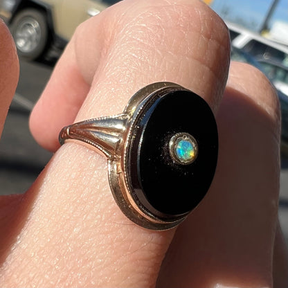A yellow gold onyx ring set with a round cabochon cut opal bezel set into the onyx.