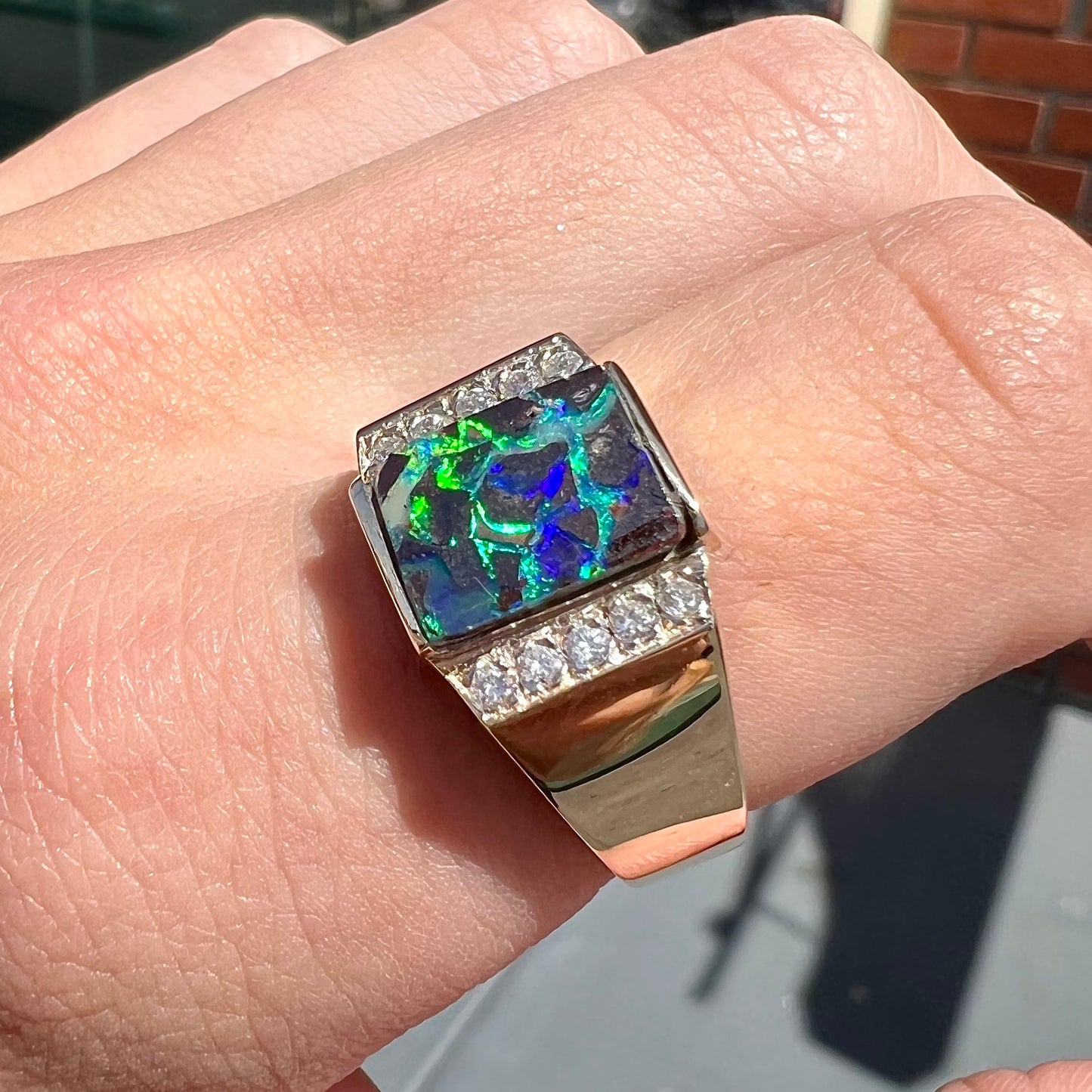 A men's gold boulder opal and diamond ring.  The opal shows blue and green colors.