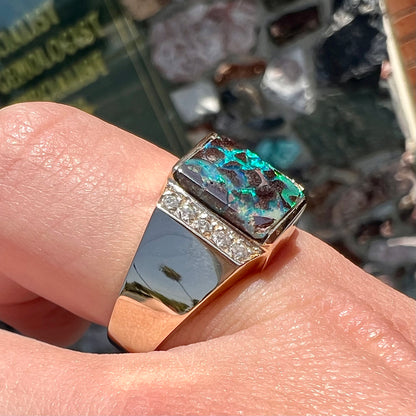 A men's gold boulder opal and diamond ring.  The opal shows blue and green colors.