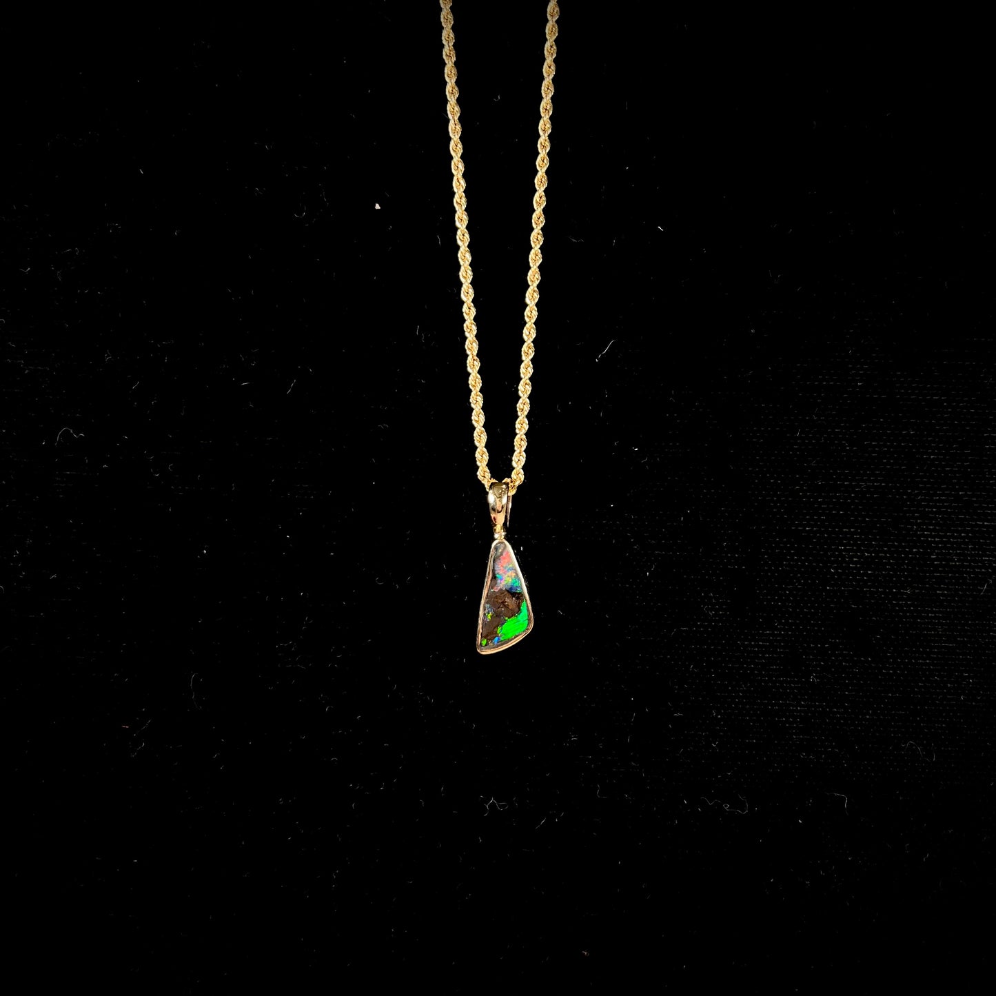 A bright green and red boulder opal bezel pendant in solid yellow gold.