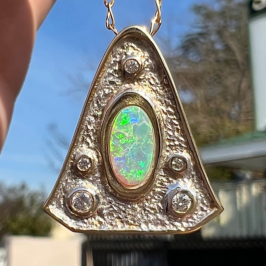 A triangular gold pendant set with five round diamonds and a white crystal opal with green fire.