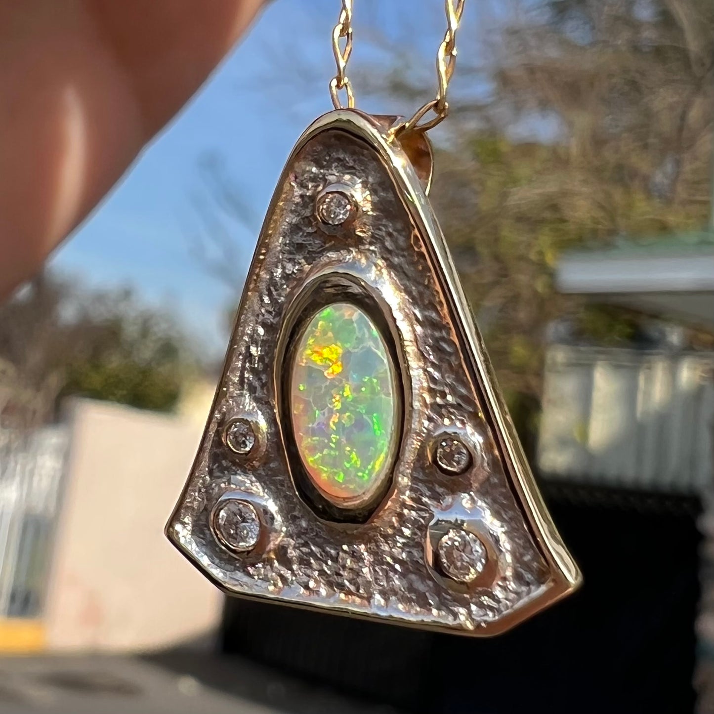 A triangular gold pendant set with five round diamonds and a white crystal opal with green fire.