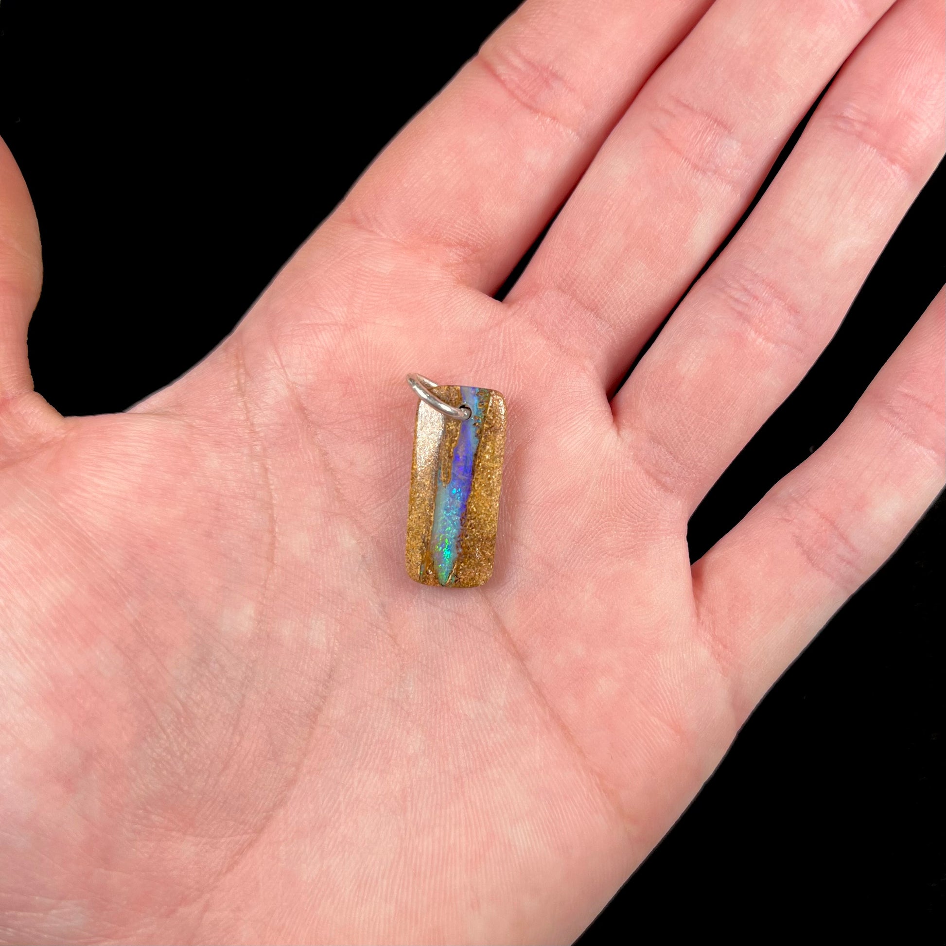 A drilled boulder opal stone with a sterling silver ring through the hole to be worn as a pendant.