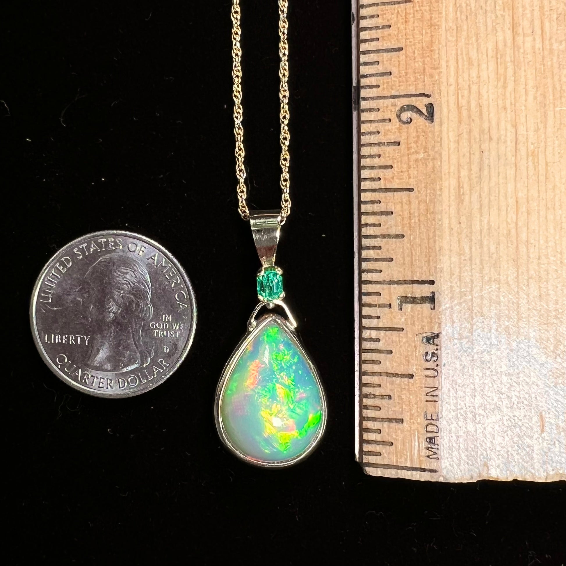 A yellow gold bezel set Ethiopian fire opal drop pendant.  There is an emerald set in the bail.