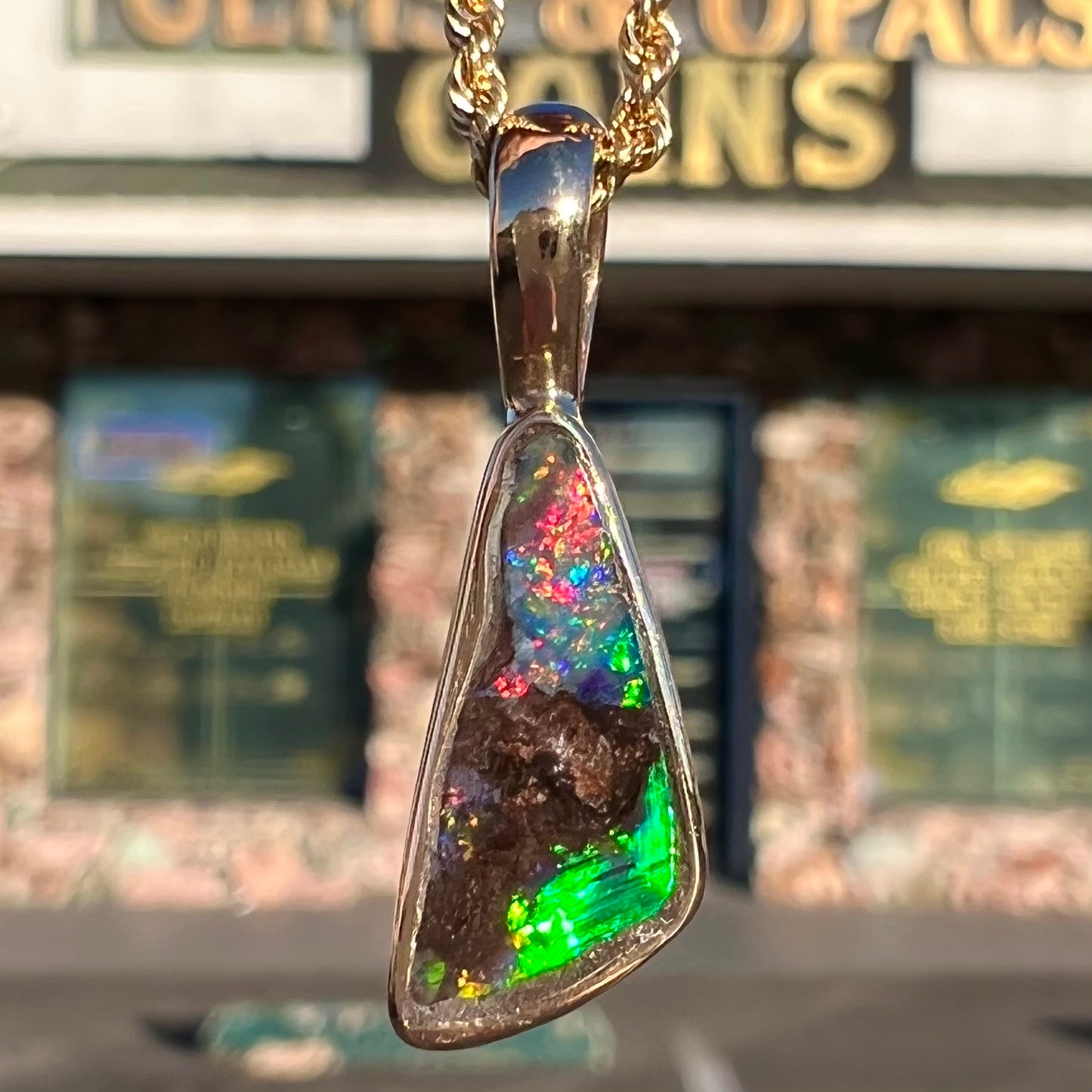 A bright green and red boulder opal bezel pendant in solid yellow gold.