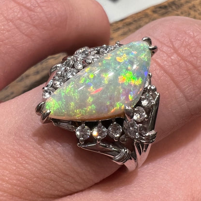 A freeform triangular cabochon cut Lightning Ridge white crystal opal set with diamonds in an ornate platinum split shank setting.