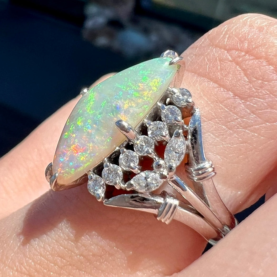 A freeform triangular cabochon cut Lightning Ridge white crystal opal set with diamonds in an ornate platinum split shank setting.