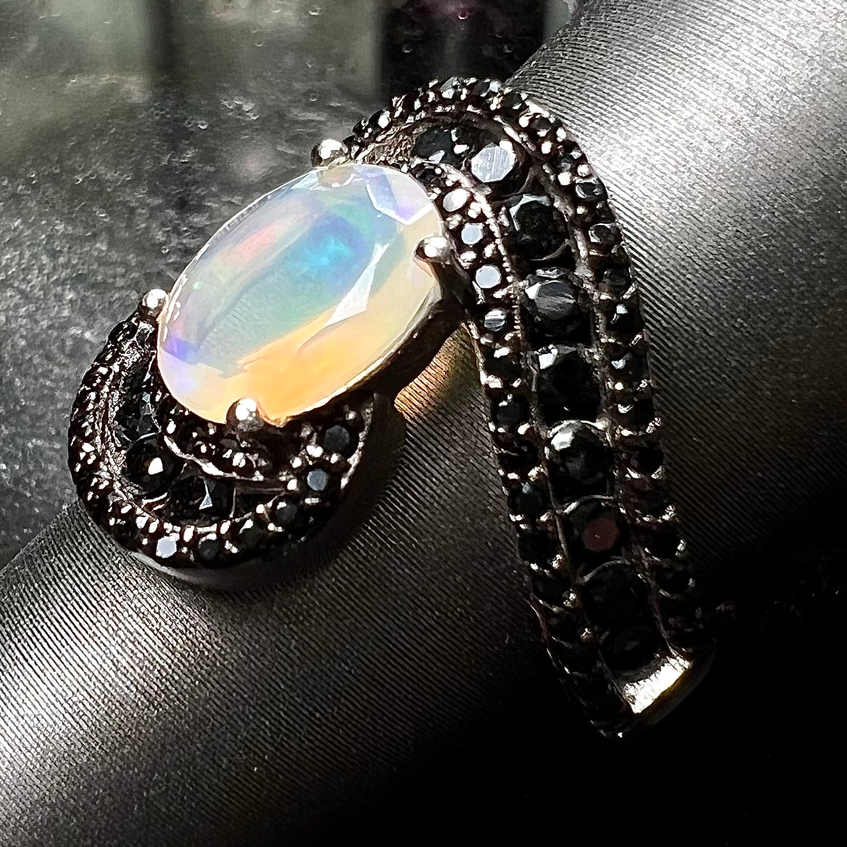A sterling silver ring set with round black spinel stones and an oval cut, faceted Ethiopian opal.