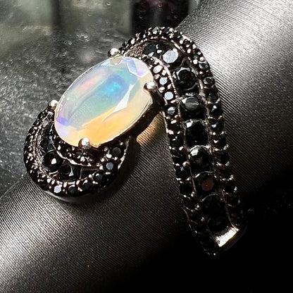 A sterling silver ring set with round black spinel stones and an oval cut, faceted Ethiopian opal.