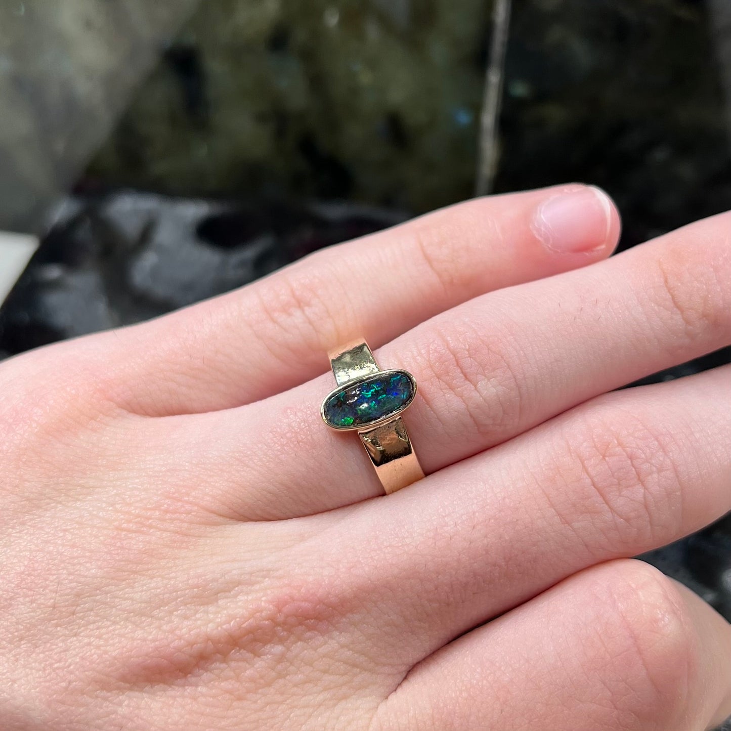 A blue green oval cabochon cut Australian boulder opal set in a yellow gold solitaire ring.