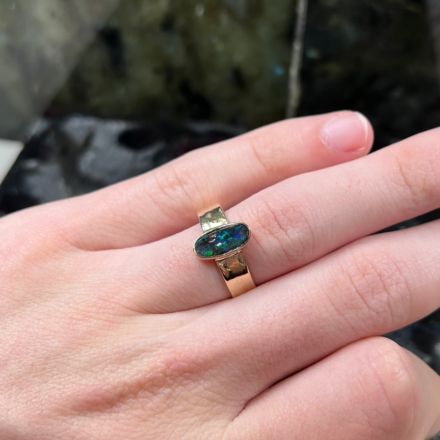 A blue green oval cabochon cut Australian boulder opal set in a yellow gold solitaire ring.