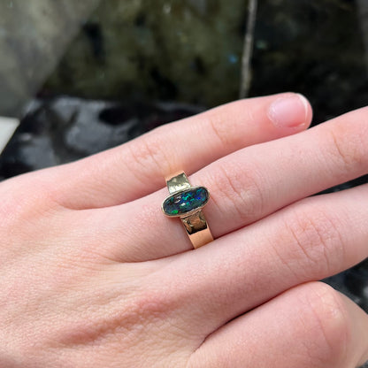 A blue green oval cabochon cut Australian boulder opal set in a yellow gold solitaire ring.