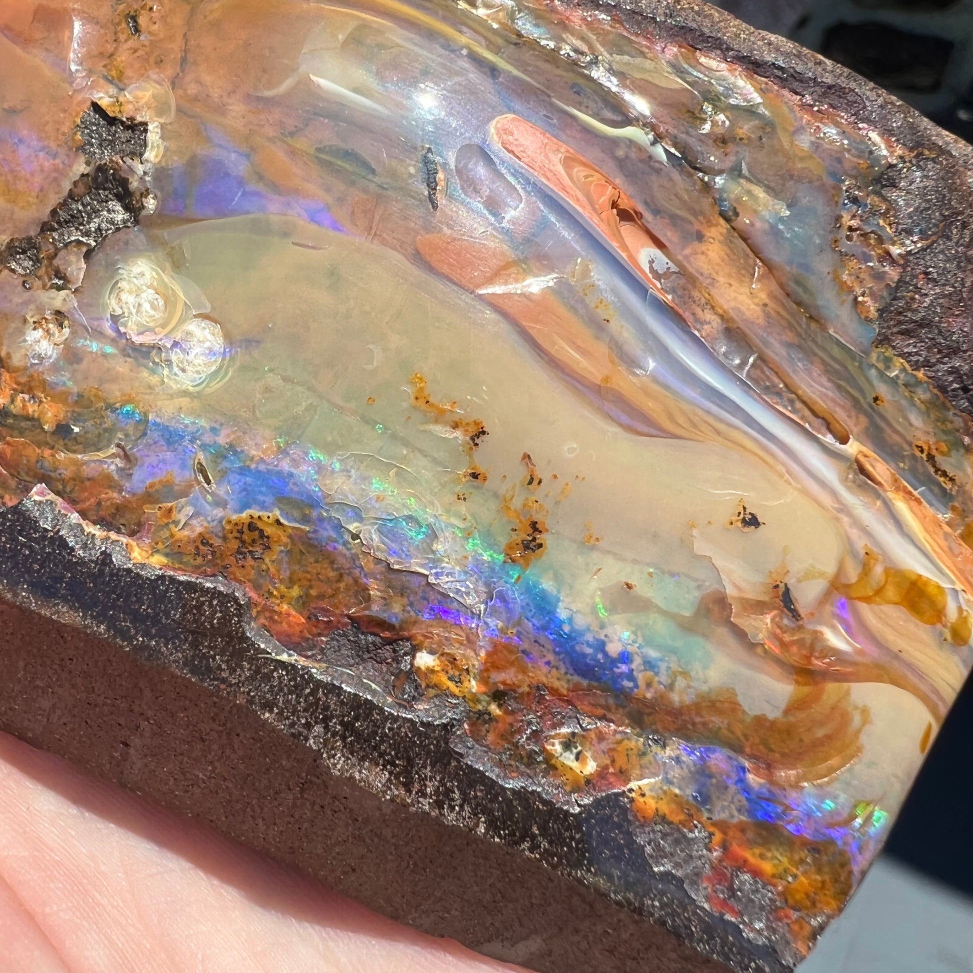 A polished Quilpie boulder opal specimen.  The stone has a stripe of bright blue, green, and purple.