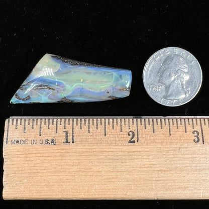 A freeform shaped, polished boulder opal stone from Queensland, Australia.  The stone has red, orange, green, and blue fire.