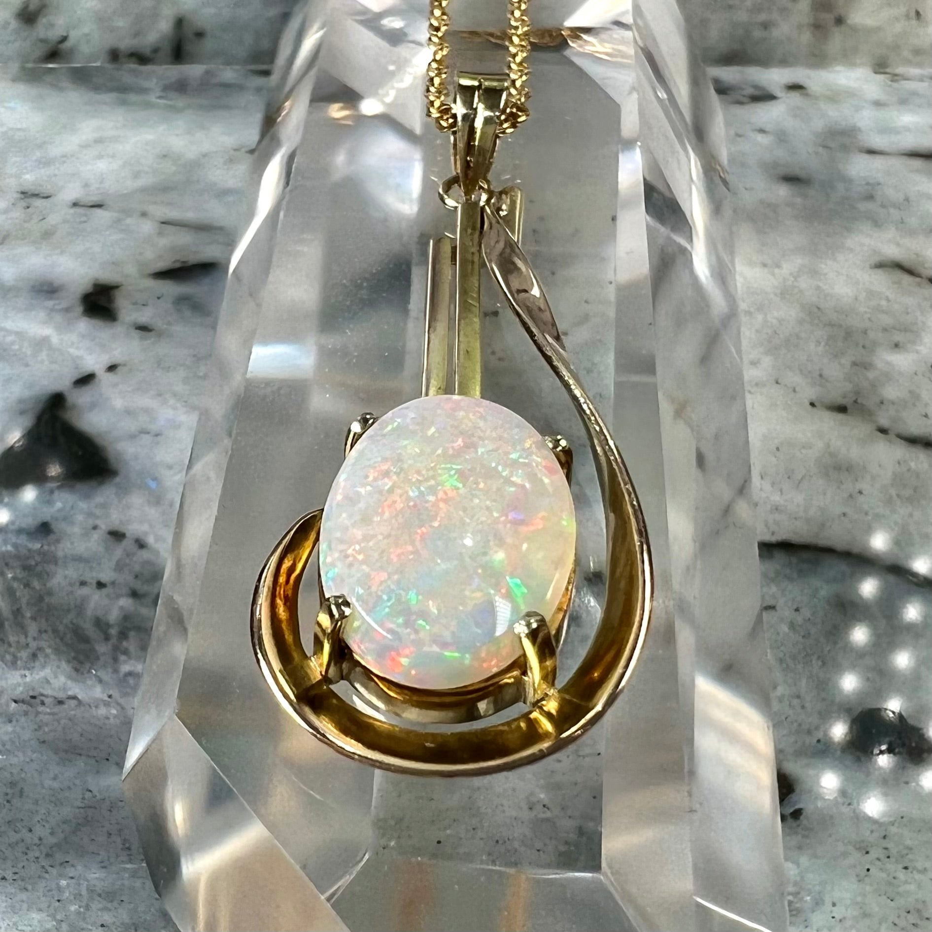 A handmade gold drop pendant set with an oval cabochon cut white crystal opal.