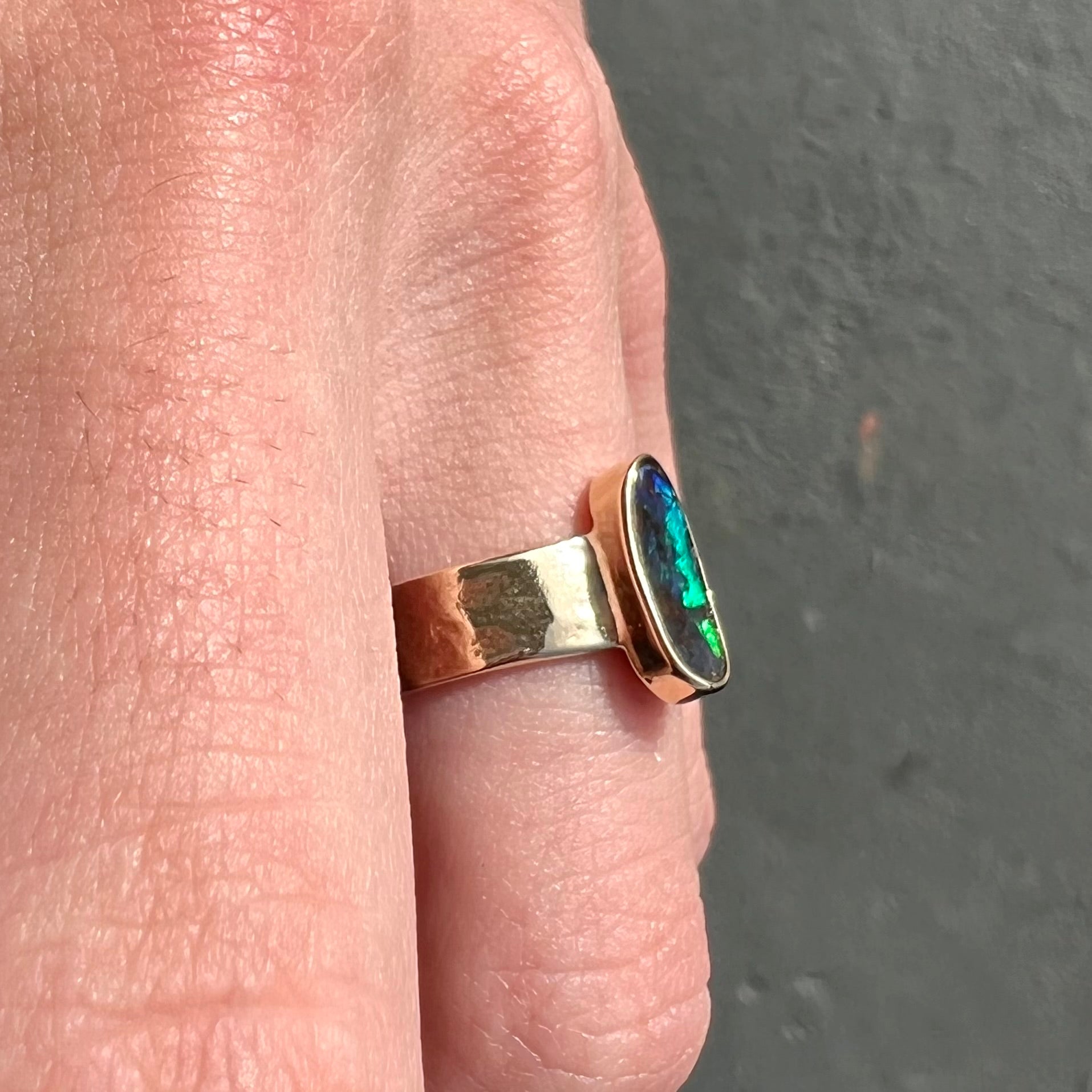 A blue green oval cabochon cut Australian boulder opal set in a yellow gold solitaire ring.