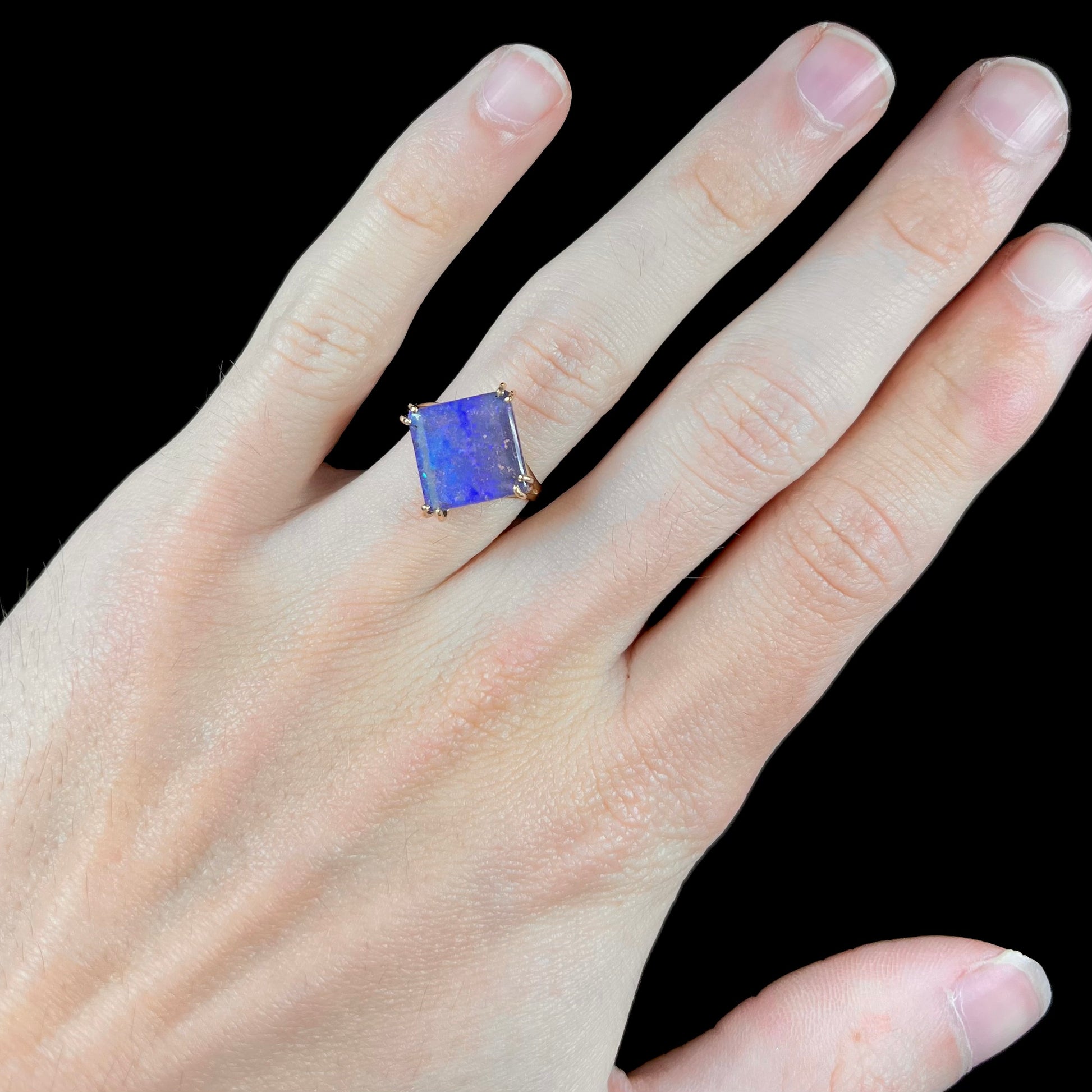 A ladies' boulder opal solitaire ring, handmade in yellow gold.  The stone is purple with flashes of blue, aqua, and green.