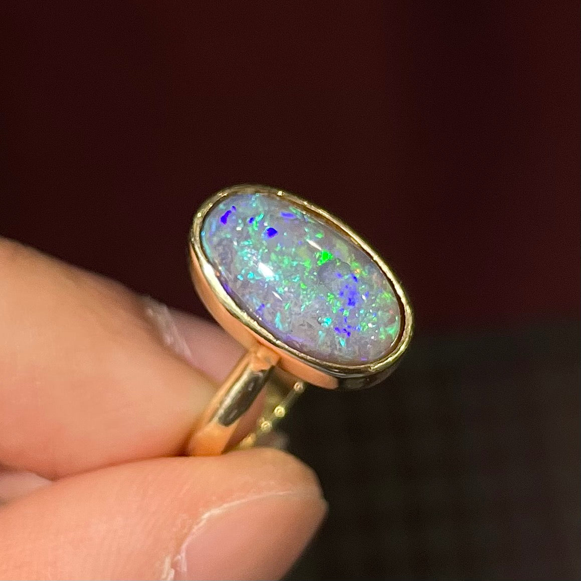 A simple yellow gold solitaire ring with a bezel set Lightning Ridge black crystal opal from Australia.