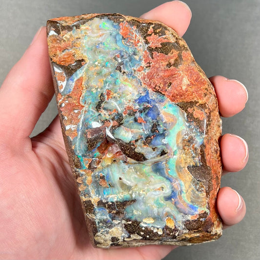 A hand-sized, polished Quilpie boulder opal specimen.  The stone shows blue, green, and orange flashes.