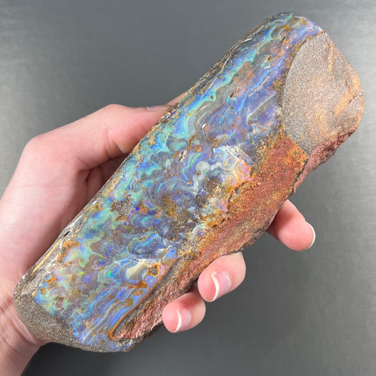 A 7 inch long, polished Quilpie boulder opal specimen.  The stone shows colors of blue, green, and orange.