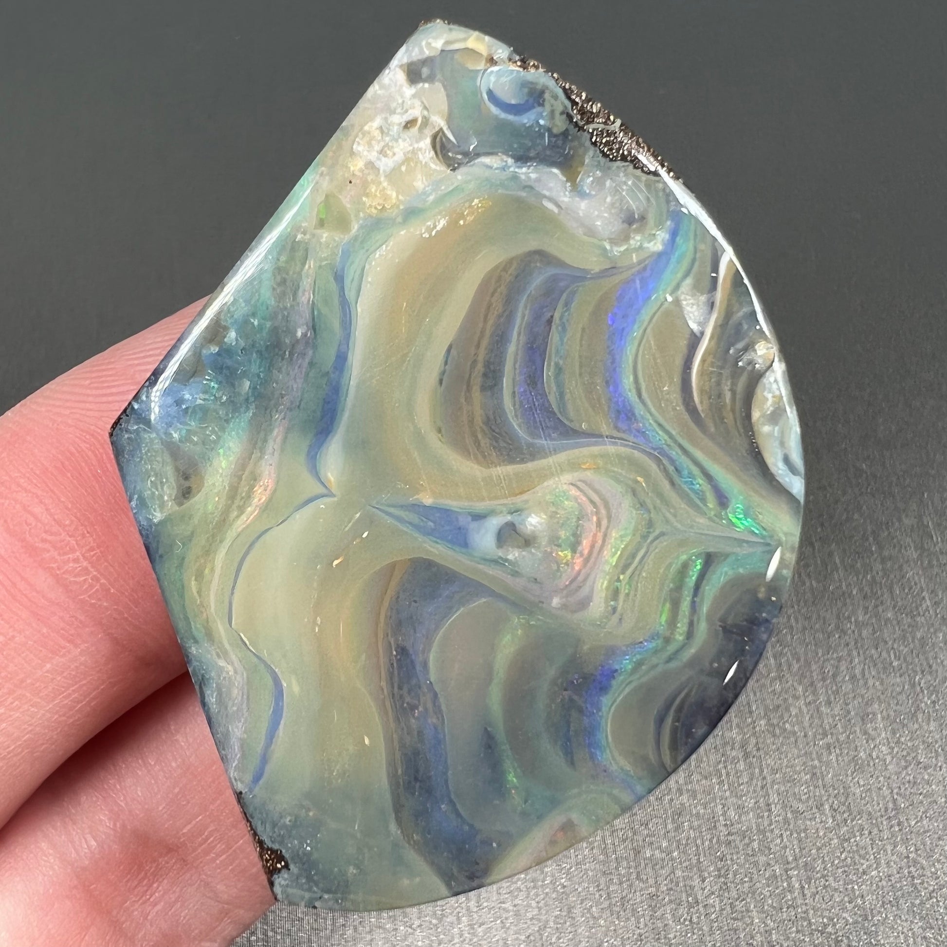 A polished, loose boulder opal stone from Queensland, Australia.  Fire colors are green, blue, purple, and salmon.