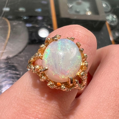 A yellow gold solitaire engagement ring set with an oval cabochon cut white crystal opal.
