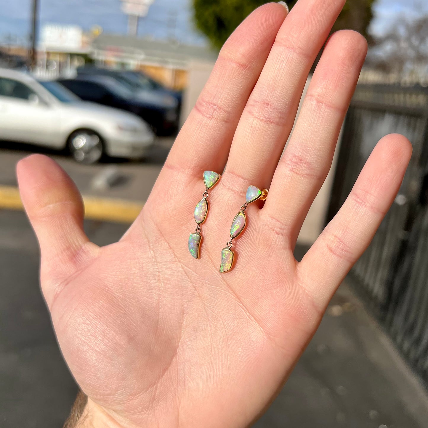 A pair of yellow gold push-back dangle earrings set with three white crystal opals in each.
