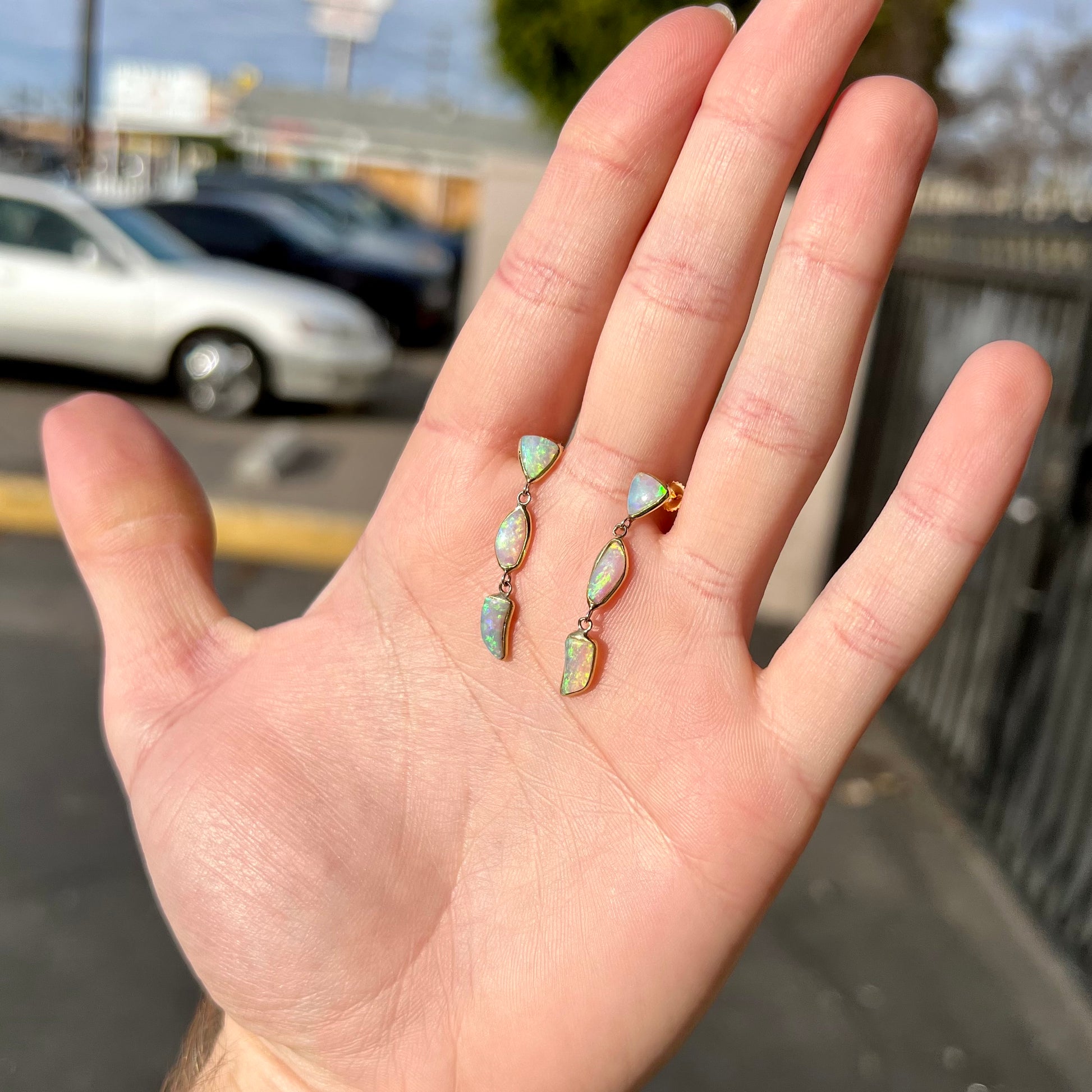 A pair of yellow gold push-back dangle earrings set with three white crystal opals in each.