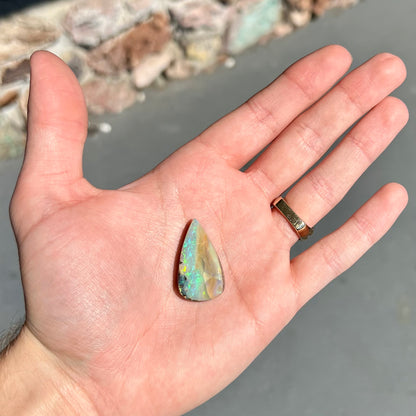 A loose, pear shaped boulder opal stone from Queensland, Australia.  Predominant colors are blue, purple, and green.