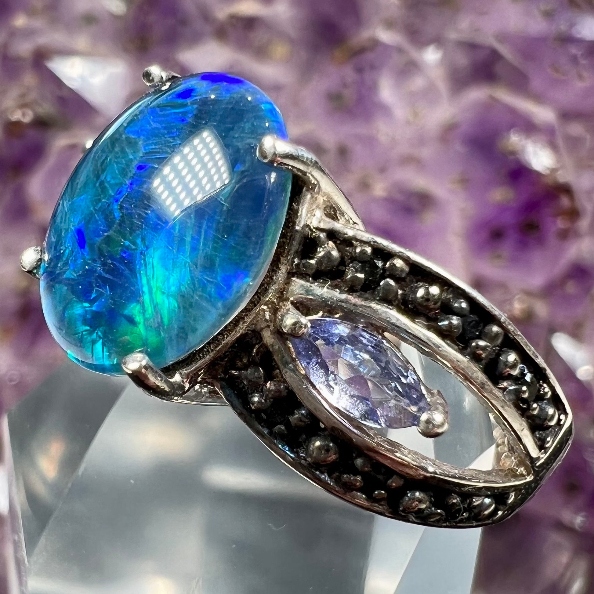 A sterling silver ring set with a black opal triplet, two marquise cut tanzanites, and round black spinel accent stones.