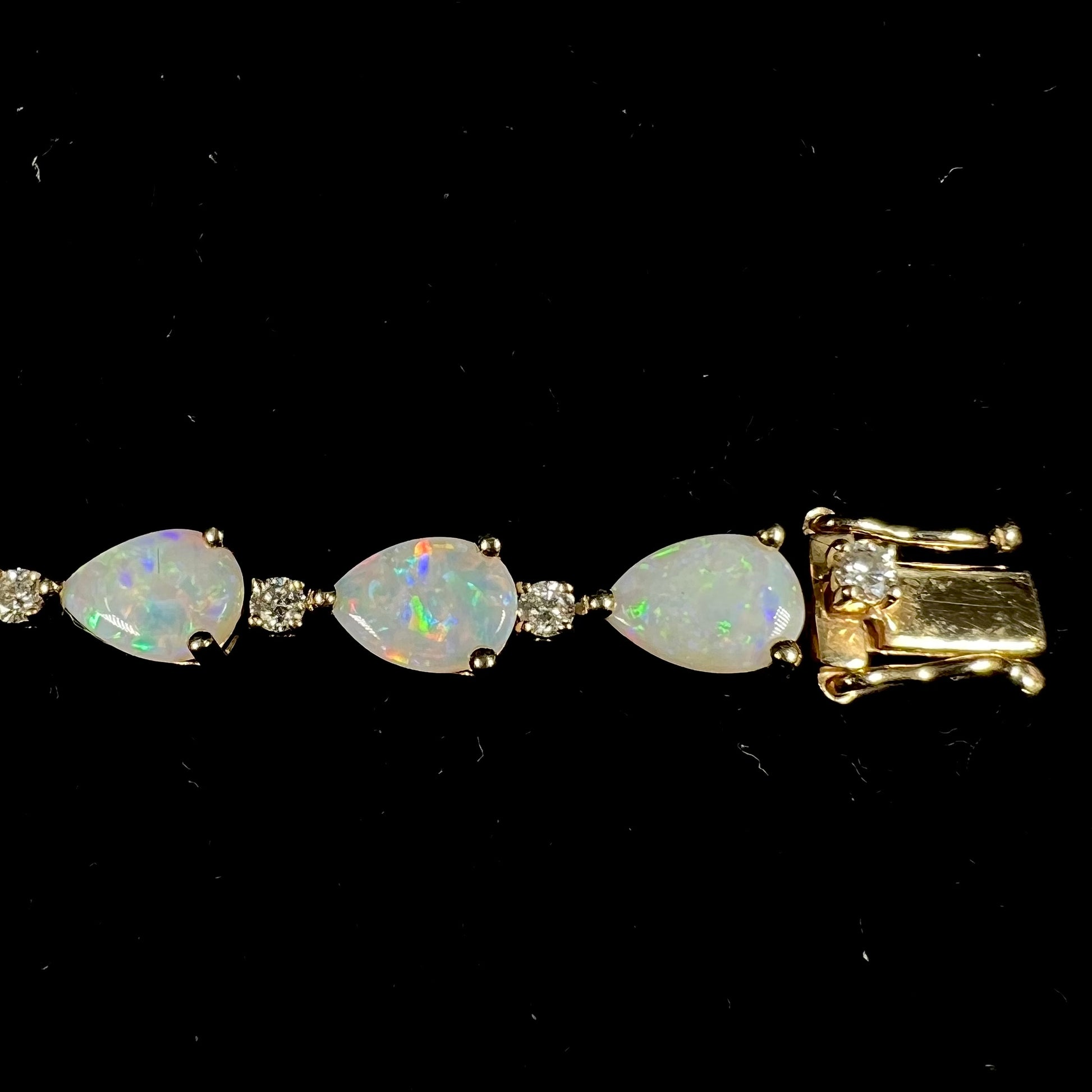 A ladies' gold tennis style bracelet set with pear shaped white crystal opals and diamonds.
