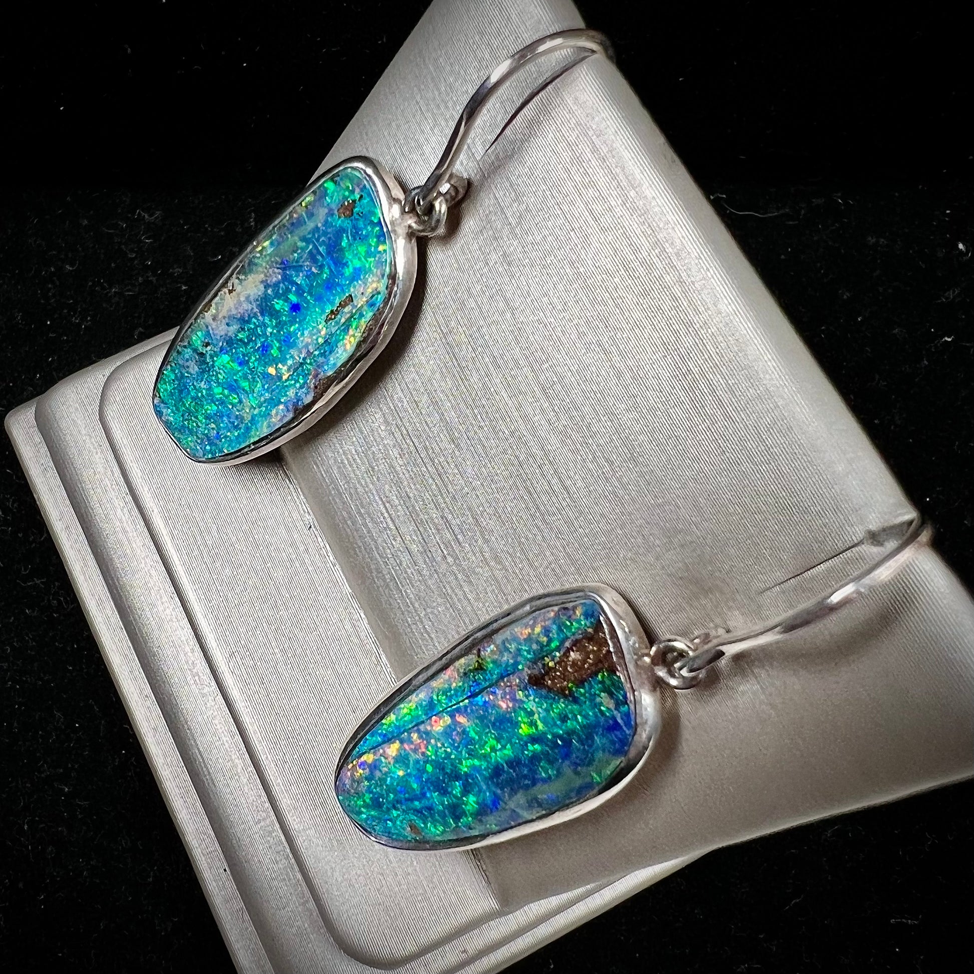 A pair of white gold boulder opal French wire dangle earrings.  The opal is predominantly glimmery blue.