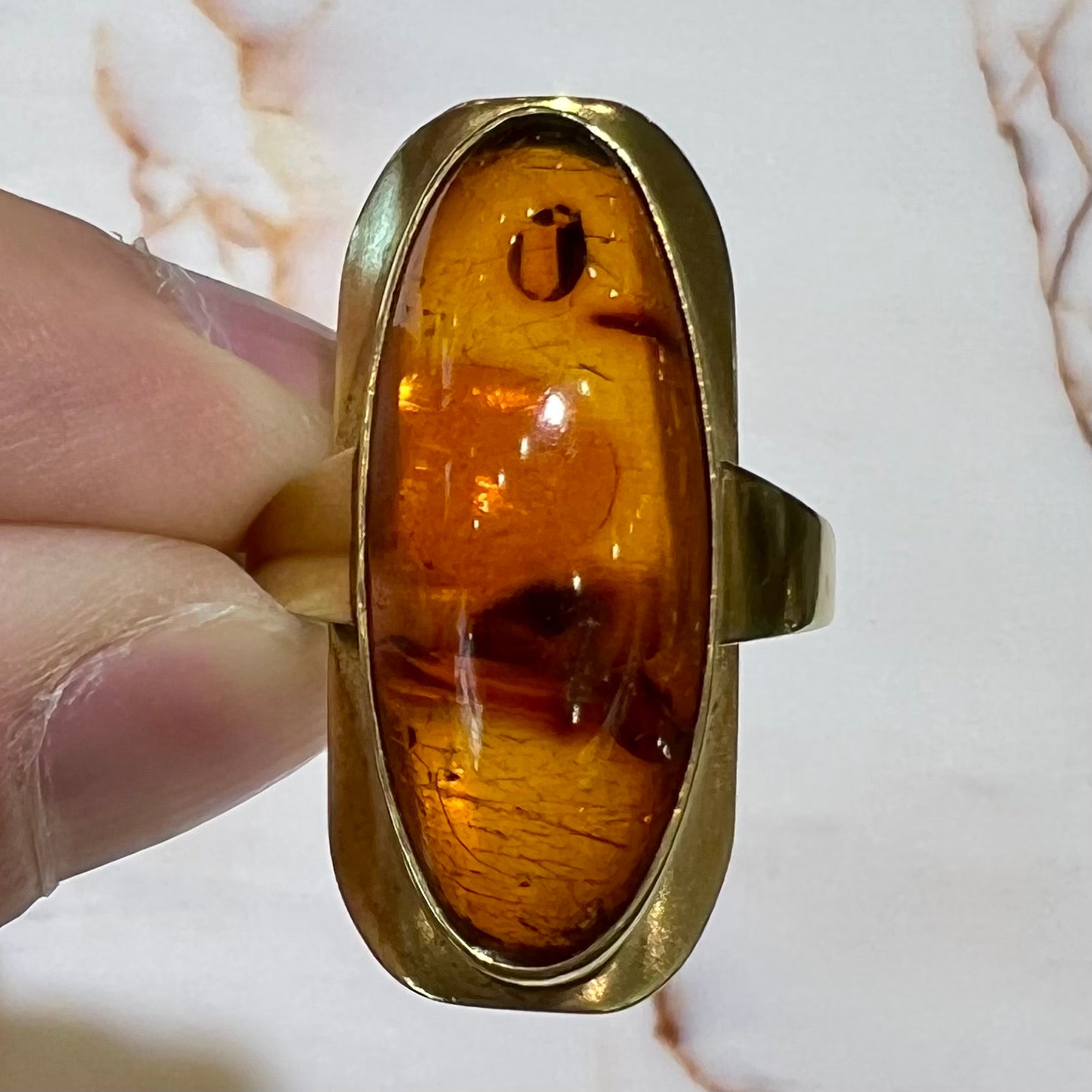 An oval cabochon cut Baltic amber stone set in a yellow gold ring and stamped "AMBER GUILD."