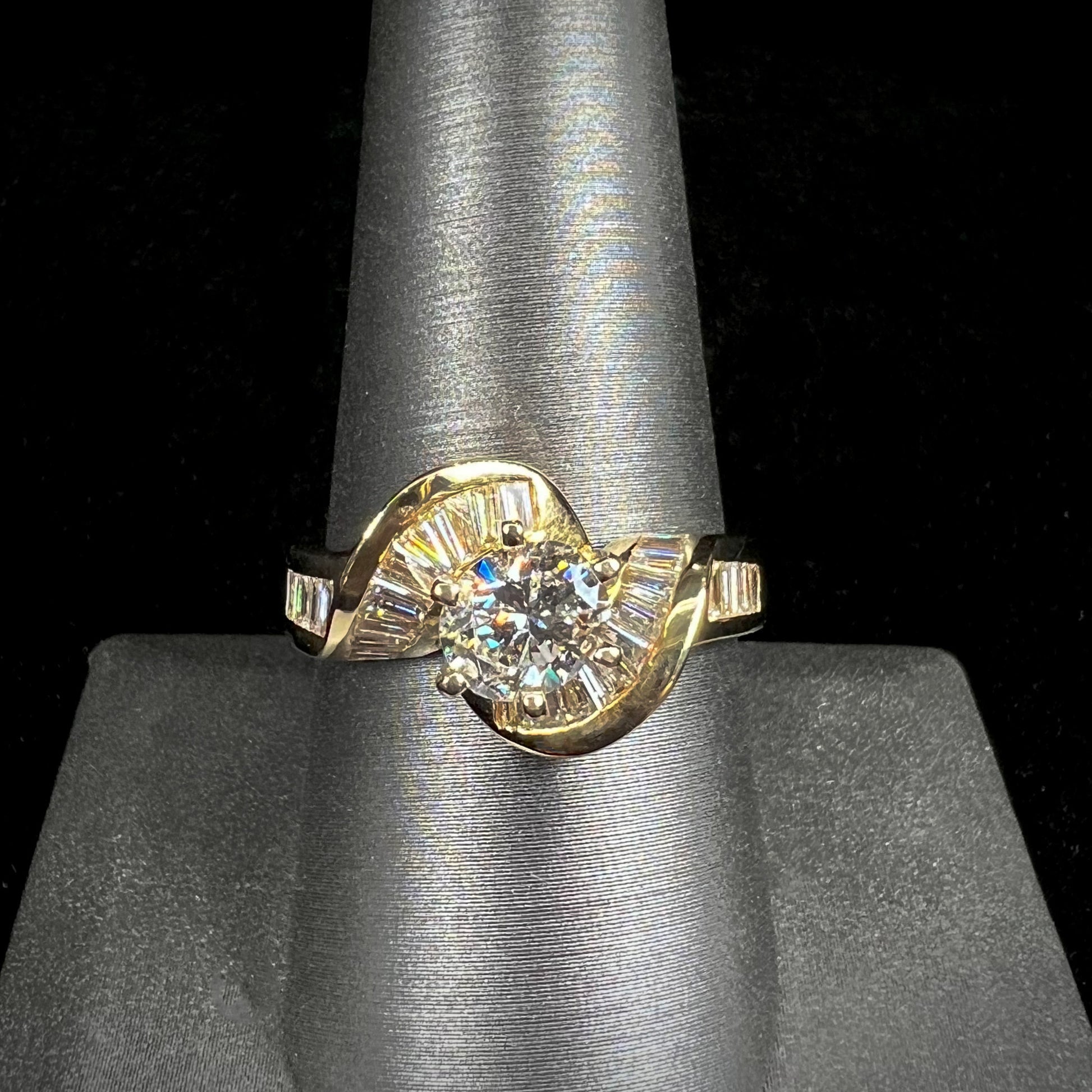 A ladies' yellow gold engagement ring set with a 0.77ct oval cut diamond and baguette cut diamond accents.