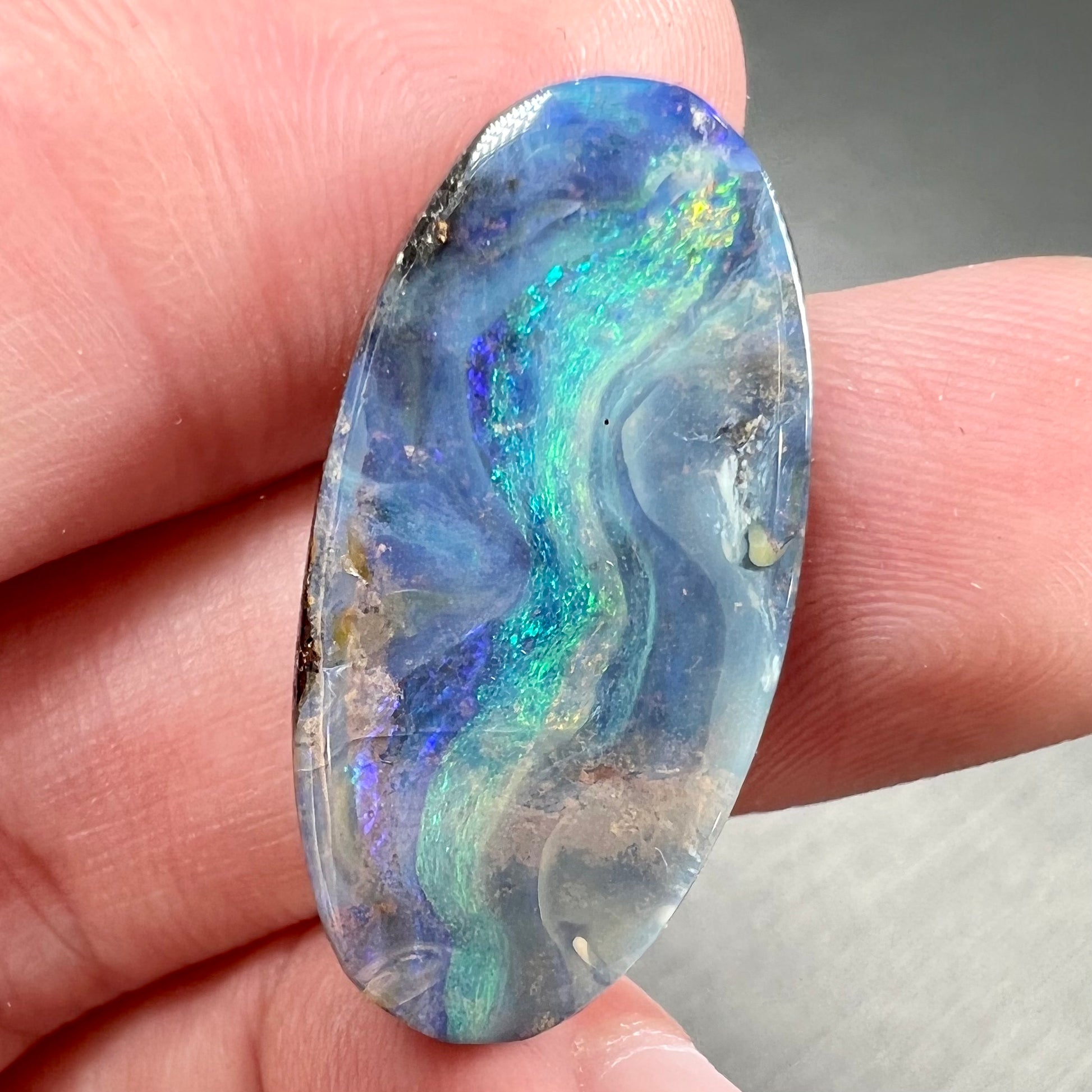 A loose, oval cabochon cut Quilpie boulder opal from Queensland, Australia.  The stone is blue with green fire.