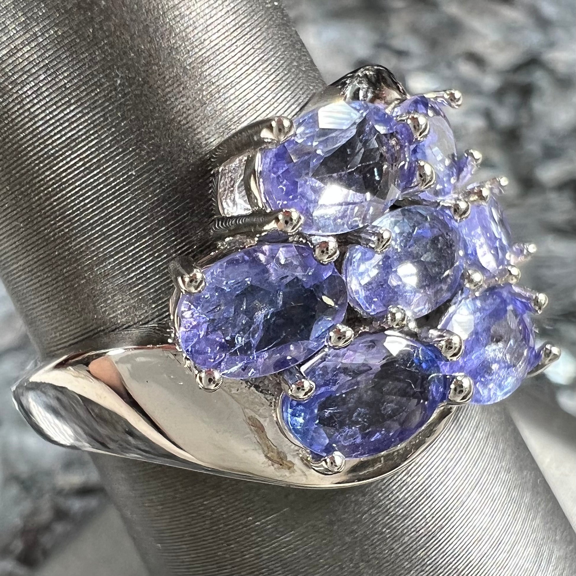 A sterling silver cluster ring prong set with seven faceted oval cut blue tanzanite stones.