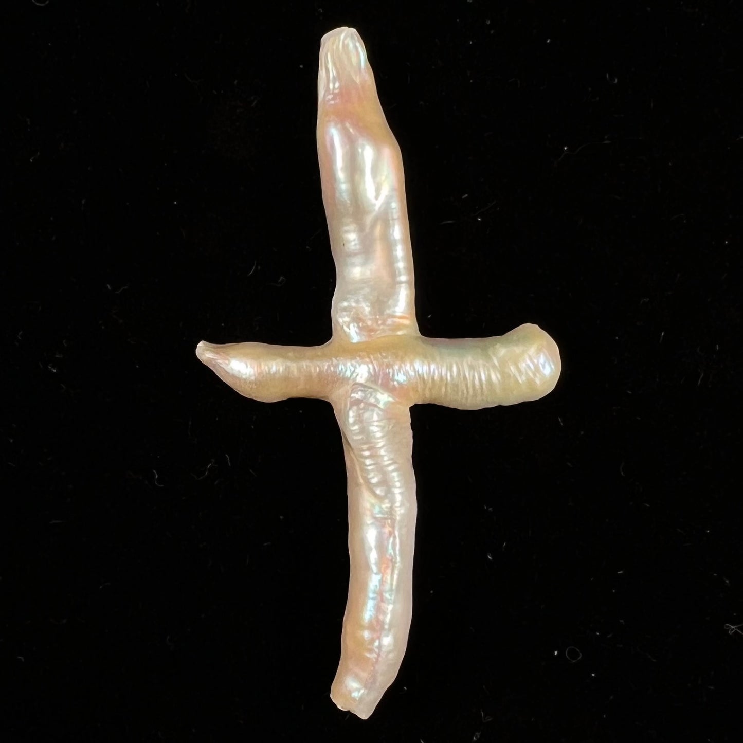 A loose, cultured dark cream colored freshwater pearl cross with pink overtones.