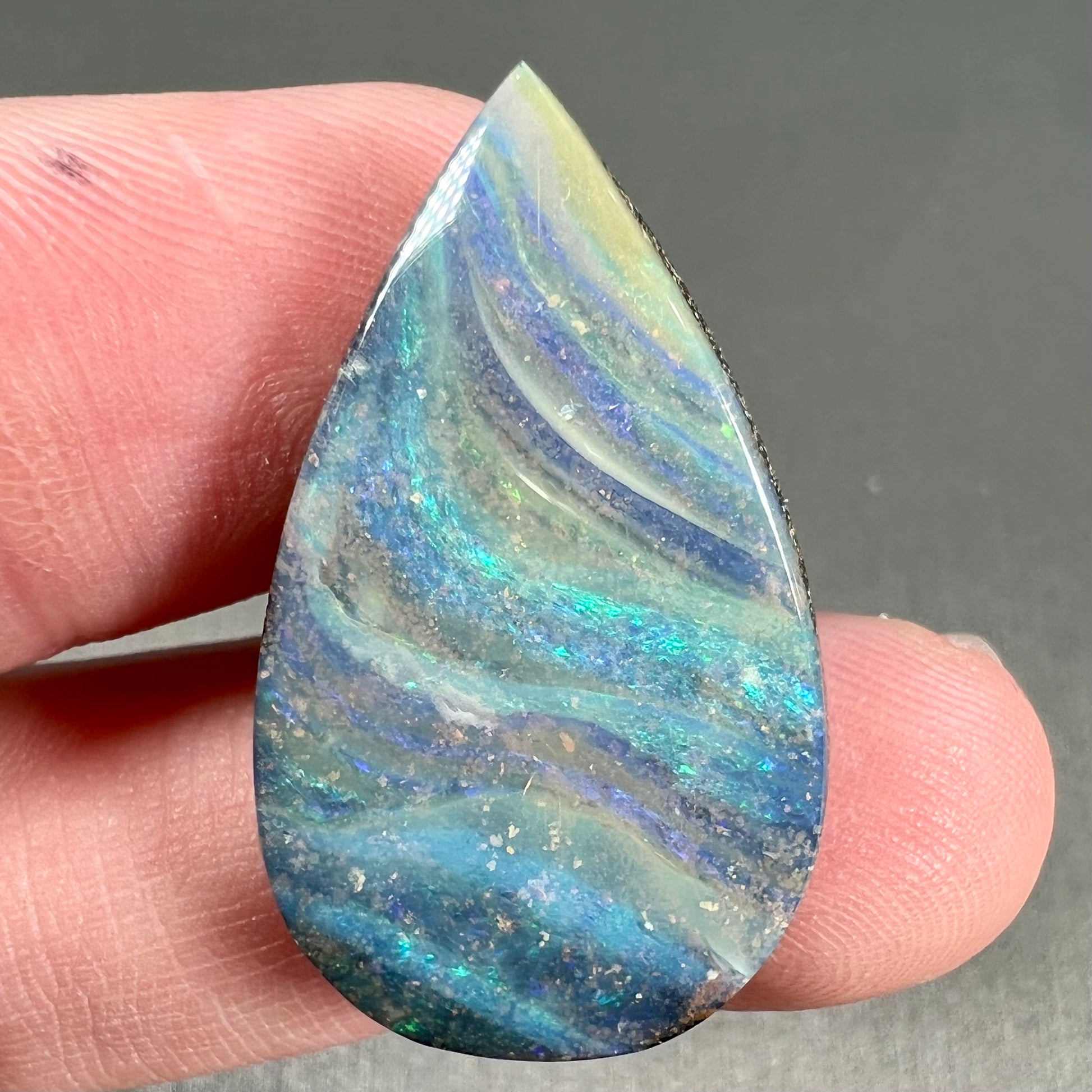 A loose, pear shaped boulder opal stone from Quilpie, Australia.  The stone is predominantly blue, green, and purple with red and orange undertones.