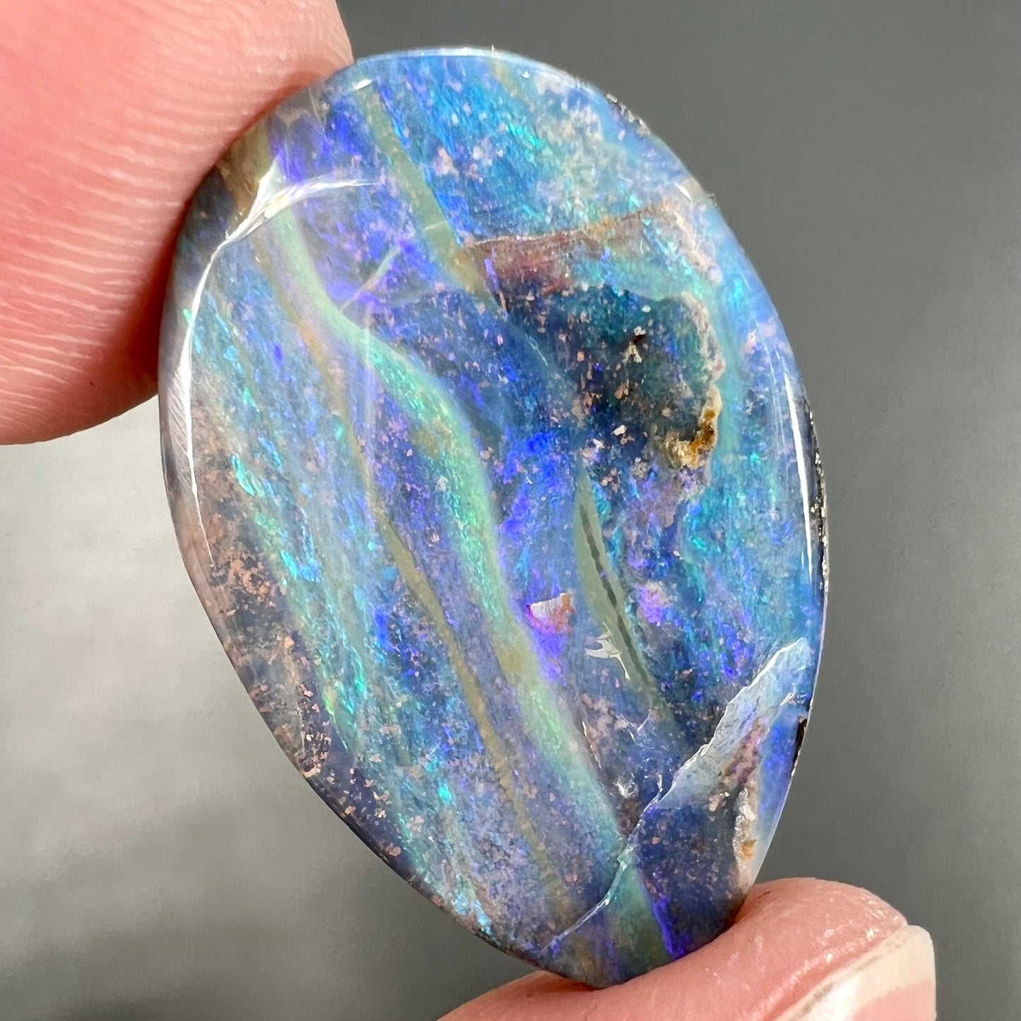 A loose, pear shaped Australian boulder opal stone.  The predominant colors are purple, green, and aqua.
