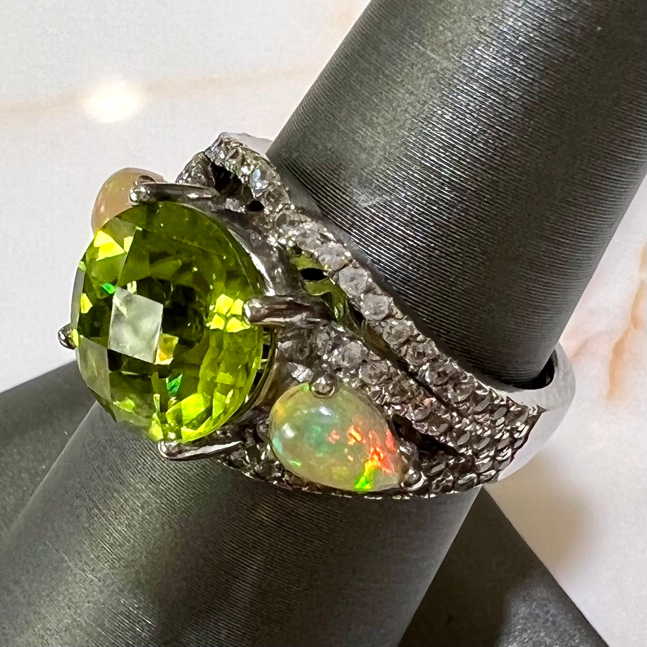 A sterling silver ring set with one large round peridot stone set between two pear shape cabochon Ethiopian opals.  Cubic zirconia stones line the ring.