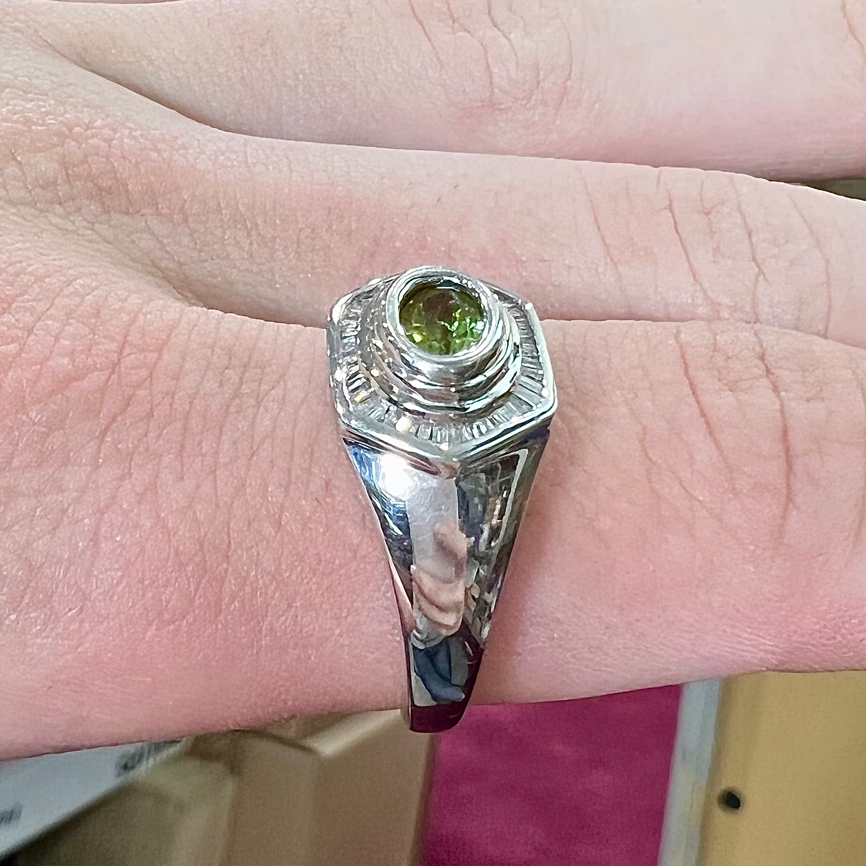 A sterling silver men's ring set with green peridot surrounded by baguette cut diamonds.